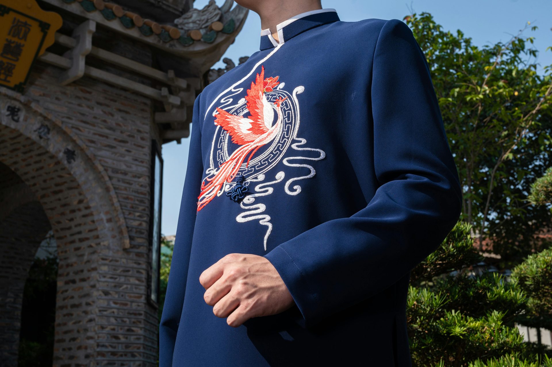 Nahaufnahme eines Mannes, der im Freien bei Sonnenschein eine traditionelle chinesische Jacke mit Vogelstickerei trägt.