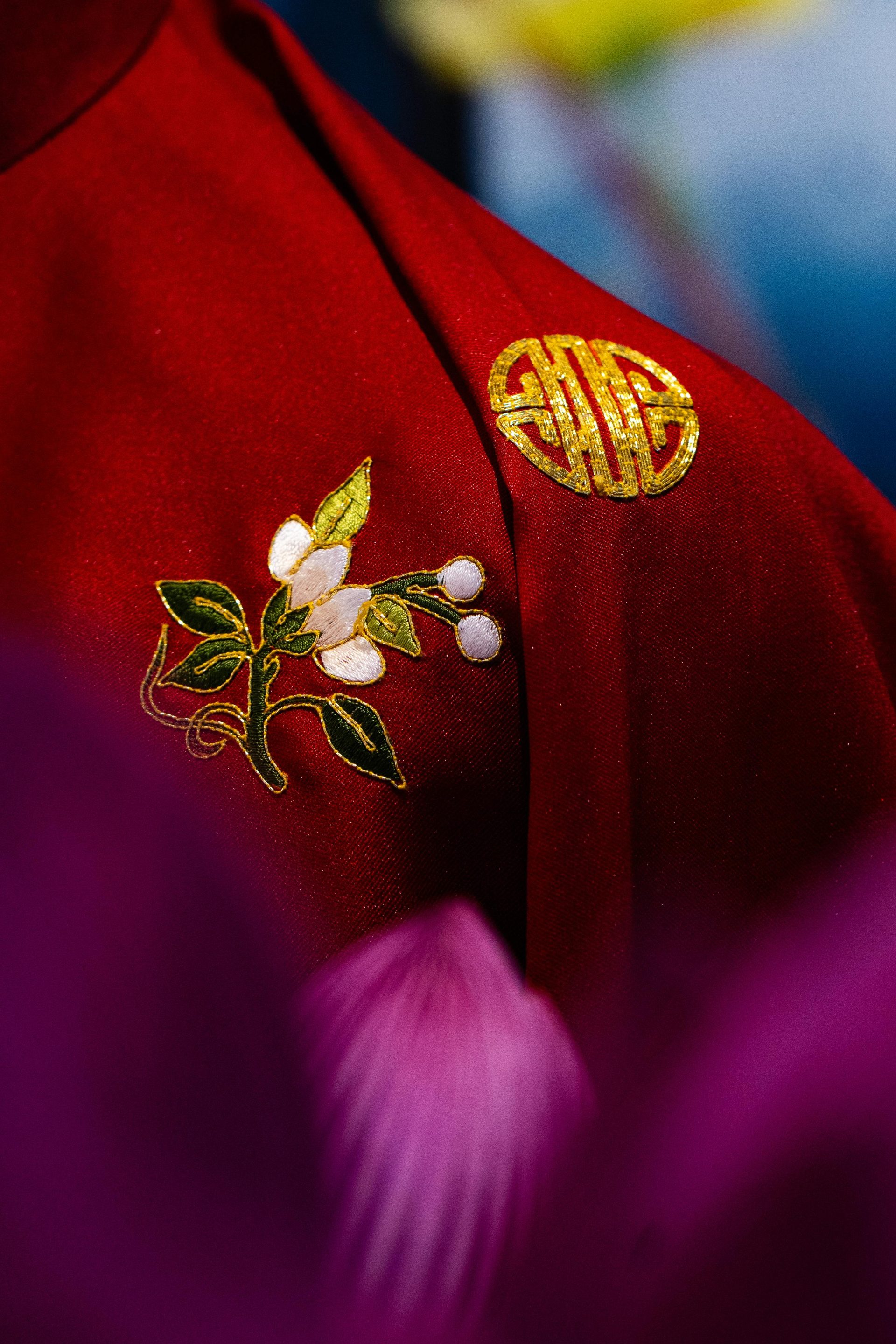 Nahaufnahme eines roten Stoffes mit aufwendiger Blumenstickerei und goldenen chinesischen Schriftzeichen.