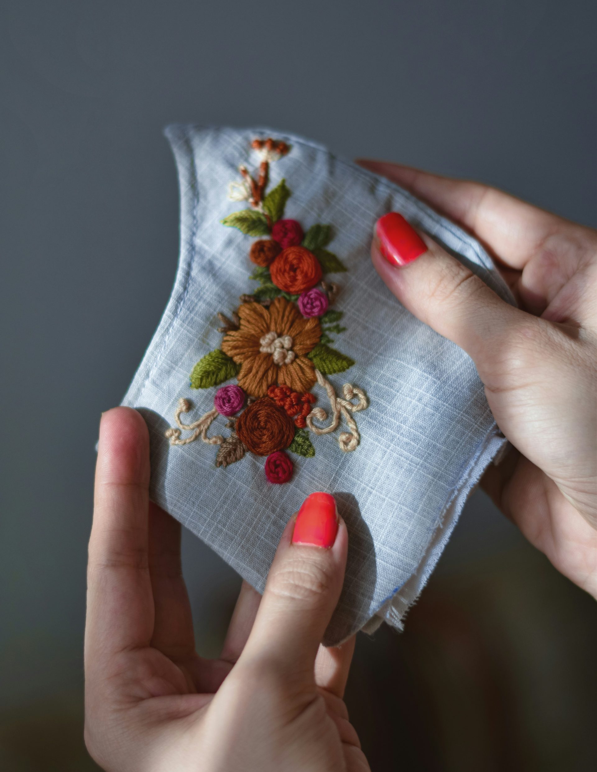 a woman's hands holding a piece of cloth with embroidered flowers on it